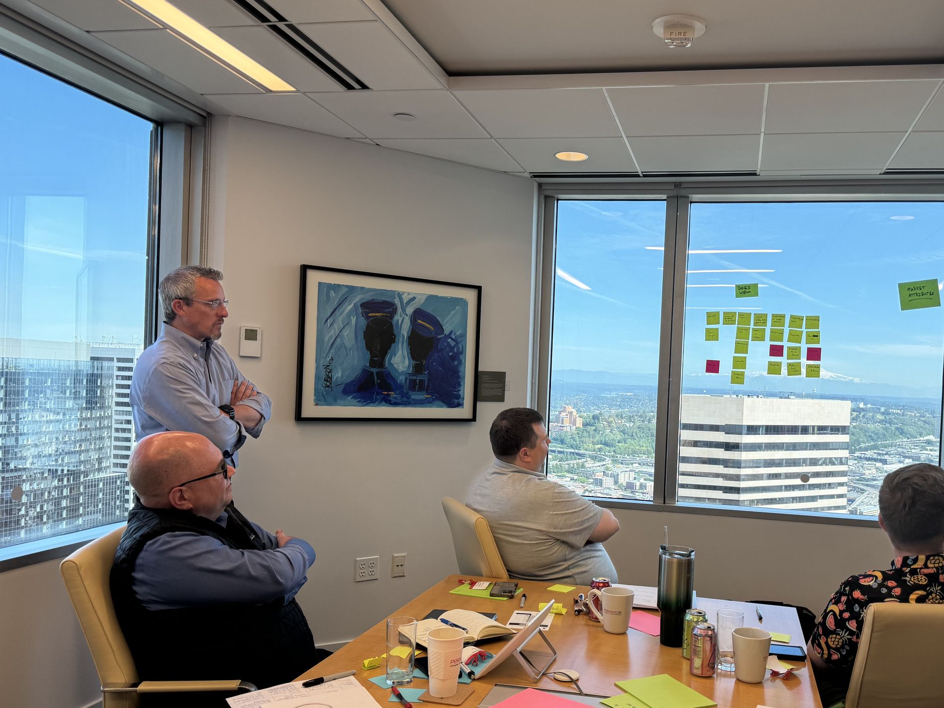 Dale Meador standing at the back of a working session, listening, while the team works a wall of notes